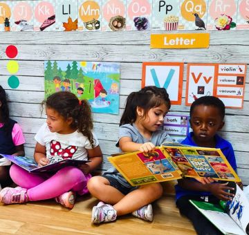Preschool children sitting on the floor reading books together in a colorful classroom at Piaget Academy, promoting early literacy and joyful learning.